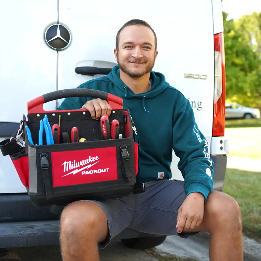 Plumber sitting on a bumper holding plumbing tools