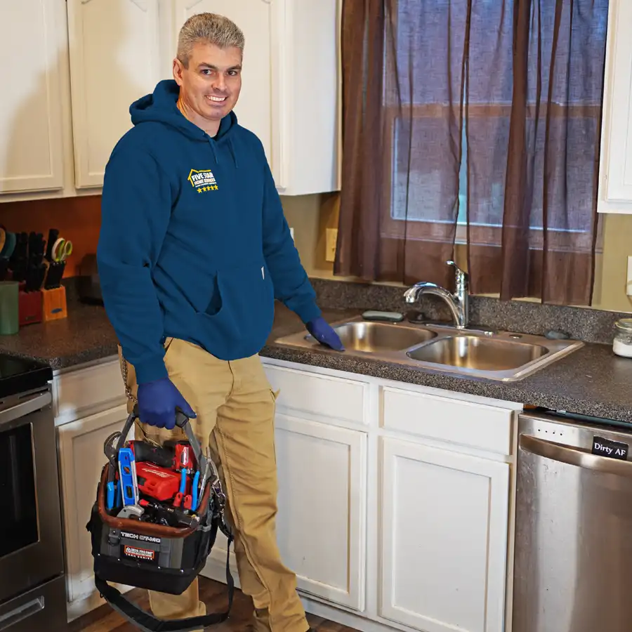 Plumber standing next to a kitchen sink holding tools