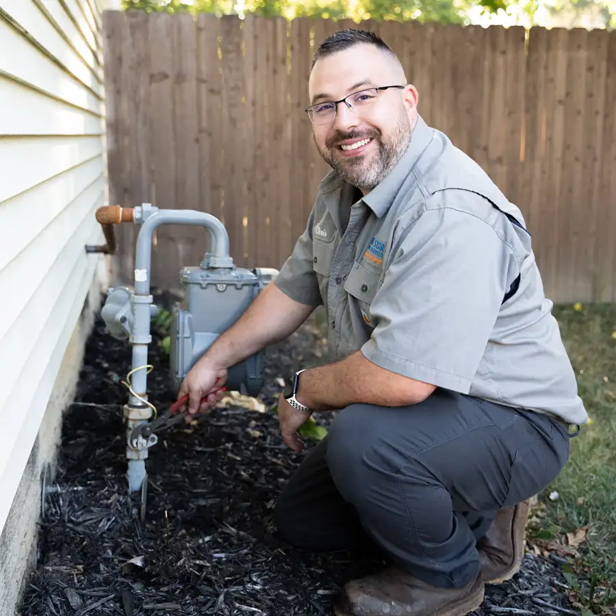 Plumbing kneeling next to a gas line meter outside of a house