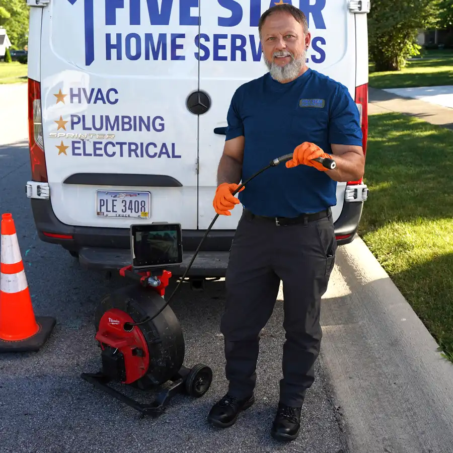 Plumber standing behind a Five Star Home Services van holding a video camera inspection unit